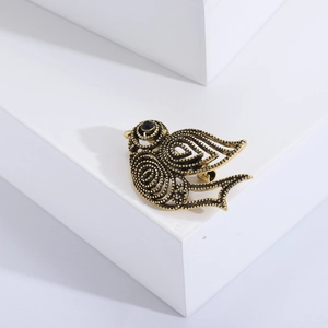 Détail d'une broche oiseau dorée vintage avec textures ciselées et œil en pierre noire