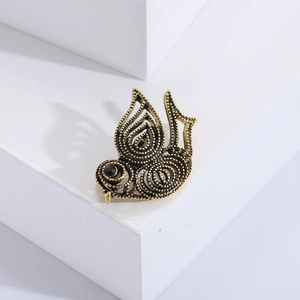 Détail de la broche oiseau vintage dorée avec motif ajouré et œil en pierre noire