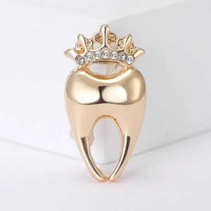 Détail d'une broche dent à couronne dorée avec strass scintillants sur socle blanc