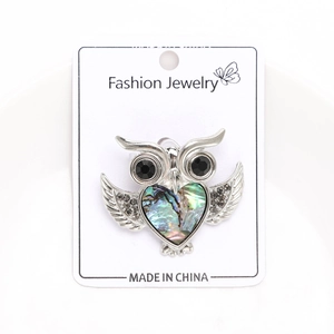 Detailed view of silver owl brooch with iridescent abalone shell heart and crystal wings