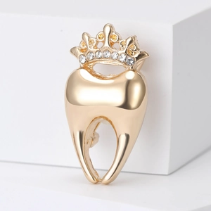 Élégante broche dent dorée avec couronne et strass brillants sur un support blanc