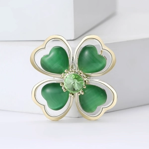 Elegant gold clover brooch with green cat-eye stones and crystal details on a white base