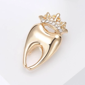 Détail d'une broche en forme de dent dorée avec couronne sertie de strass brillants