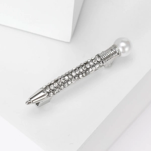 Macro shot of silver quill brooch with rows of sparkling crystals and a white pearl detail
