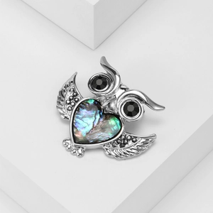 Elegant owl brooch with abalone shell heart and black crystals on a white pedestal