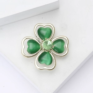 Elegant gold clover brooch with green cat-eye stones on a white artistic display block