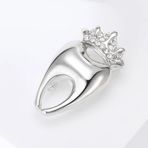Détail de la broche en forme de dent argentée avec couronne et strass en cristal brillant