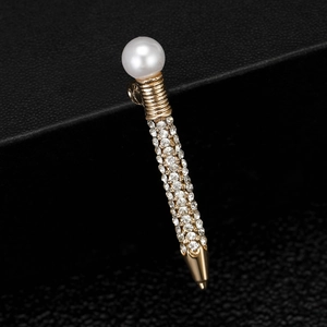 Macro detail of gold pen brooch with white pearl and sparkling inlaid rhinestones