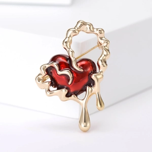 Macro detail of red enamel heart brooch with wavy gold metal frame and water drop pendant