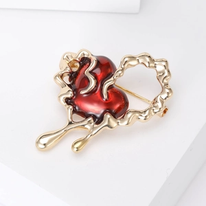 Detailed view of heart-shaped gold-tone brooch with red enamel in a fluid melting design