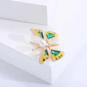 Détail d'une broche papillon dorée avec émail vert et jaune et incrustation de perle blanche
