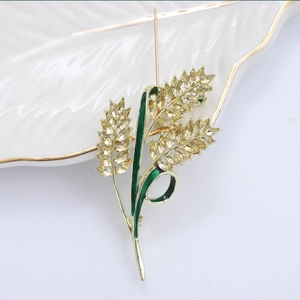 Dettaglio spilla a spiga di grano con strass gialli e smalto verde su piatto di ceramica