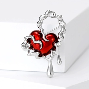 Macro detail of molten silver frame and glossy red enamel heart brooch on white pedestal