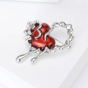 Macro detail of wave-shaped silver brooch featuring a translucent red resin heart core
