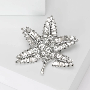 Macro detail of silver maple leaf brooch with sparkling zircons on white platform