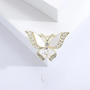 Detalle de un broche de mariposa dorado con alas blancas y cristales brillantes