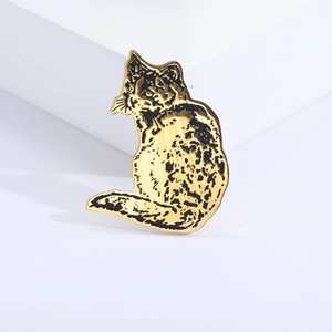 Macro detail of golden stainless steel cat brooch with brushed texture and black spots