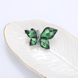 Detailed macro view of butterfly brooch with green crystals on a ceramic leaf tray