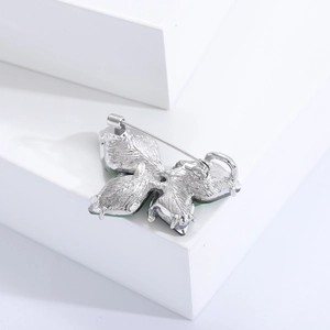 Back view of silver butterfly brooch with green crystals and metal pin on white steps