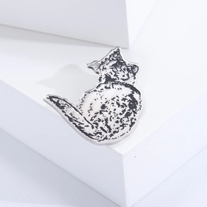 Macro view of silver cat brooch with black enamel details on white geometric stand
