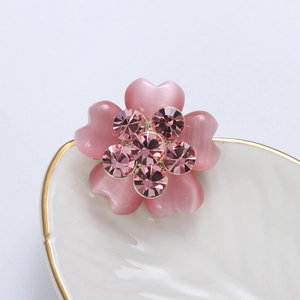 Detailed close-up of a pink rhinestone flower brooch with opal petals on a heart plate