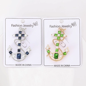 Detail view of anchor brooches with emerald crystals and pearls on display card
