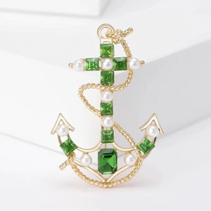 Detail of vintage anchor brooch with green gemstones and white pearls on golden base