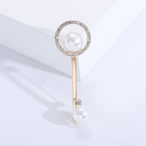 Elegant gold key brooch with pearls and rhinestones on white minimalist background