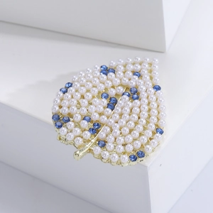 Détail d'une broche feuille dorée avec cristaux bleus et perles blanches sur support