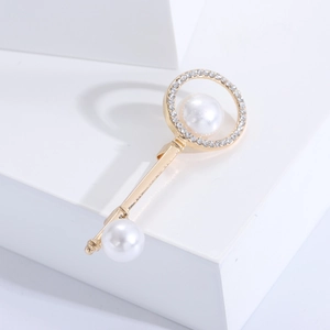 Macro detail of a gold key brooch with pavé diamonds and dual white pearls on a white block