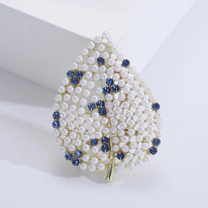 Détail macro d'une broche en forme de feuille avec cadre doré, perles et cristaux bleus