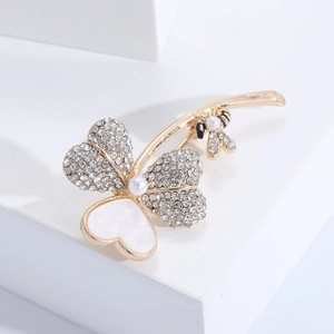Détail macro d'une broche trèfle dorée avec cœur en nacre, cristaux et petite abeille