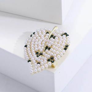 Détail de la broche feuille ajourée avec perles blanches et gemmes vert foncé sur base dorée