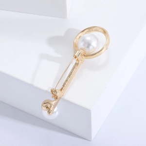 Macro detail of a golden key brooch with white pearls on a geometric display