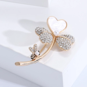 Détail d'une broche trèfle dorée avec cœur en nacre, cristaux et petit motif d'abeille
