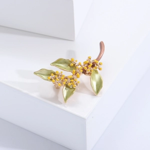 Dettaglio dell'elegante spilla osmanthus con foglie in smalto verde e perle gialle su oro