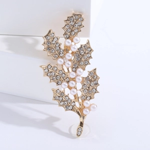 Détail de la broche feuille de houx dorée avec strass brillants et perles blanches