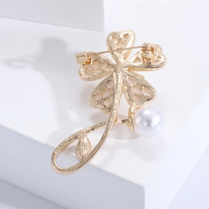 Detail of elegant gold flower brooch featuring hollow heart petals and a white pearl accent