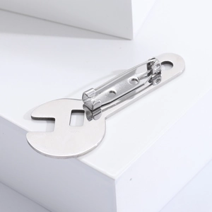 Detailed view of wrench-shaped stainless steel brooch on a minimalist white pedestal
