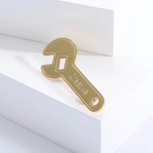 Macro detail of a golden wrench brooch featuring an engraved creative text on white stairs