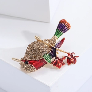 Détail de la broche colibri avec des fleurs en émail coloré et des strass étincelants