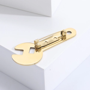 Macro detail of a golden wrench shaped brooch featuring a polished metallic mirror finish