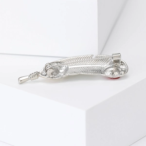 Elegant silver feather brooch with red gemstone accent shown from a detailed side angle view