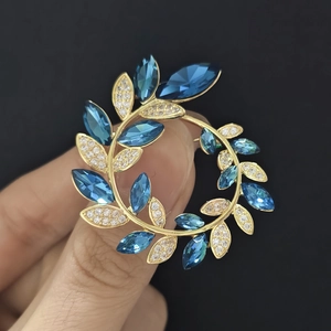 Vue macro d'une broche couronne d'olivier dorée avec cristaux bleus et zircons