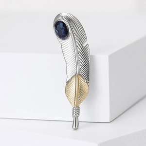 Elegant gold and silver feather brooch with a deep blue oval gemstone and spiral detail
