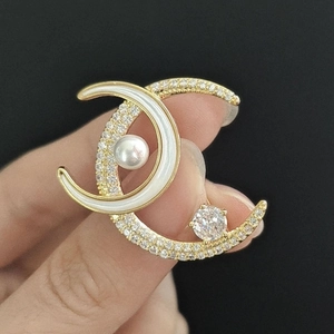 Detail of gold double C brooch with micro-paved zircons and a large white pearl