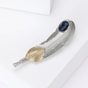 Detailed view of feather brooch featuring gold and silver tones with blue gemstone