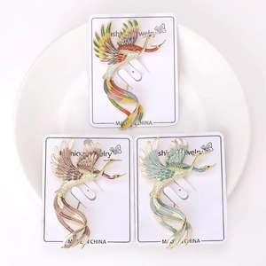 Detail of colorful enamel phoenix brooches with cubic zirconia on a white plate