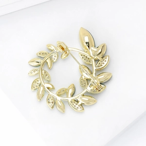 Broche couronne de feuilles dorées avec incrustations de zircons étincelants sur fond blanc