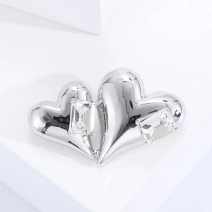 Détail d'une broche double cœur argentée avec pierres zircons sur support blanc
